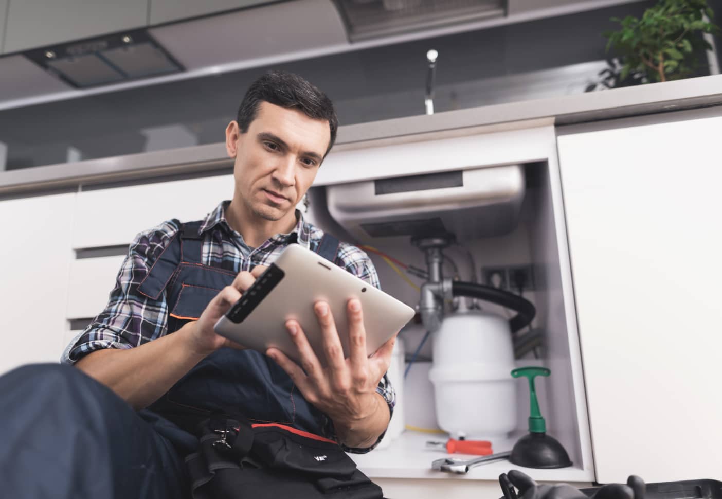 Plumber viewing instructions on tablet while fixing kitchen sink